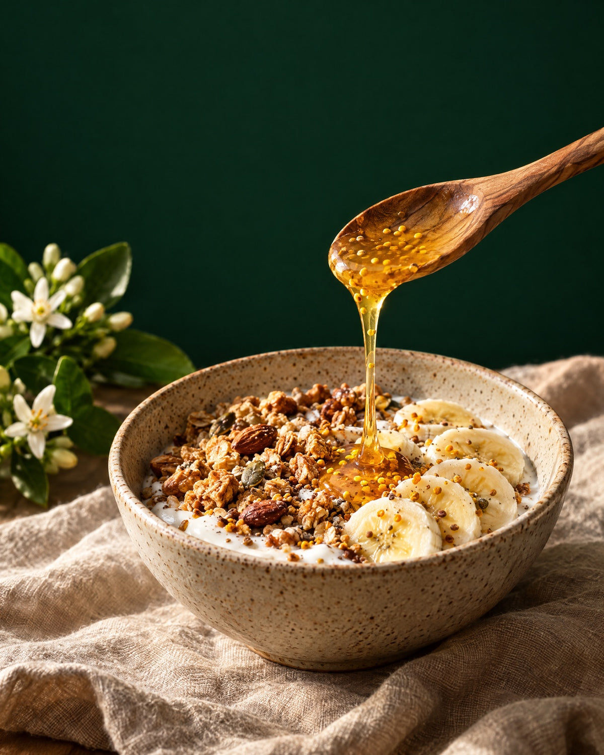 Tazón de yogur con granola y banano; una cuchara de madera deja caer miel